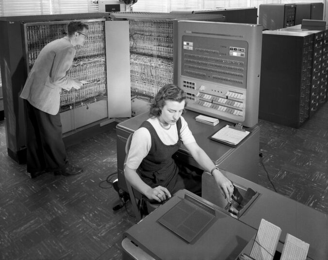 Two people working with an IBM 704 computer at NACA Langley in 1957, one at the open cabinet, one at the card reader
